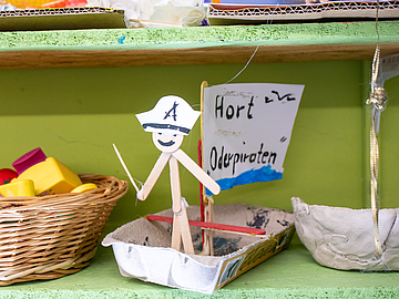 Gebasteltes Piratenschiff mit der Aufschrift „Hort Oderpiraten“ steht auf einem Regal neben einem Korb mit buntem Spielzeug und weiteren Bastelarbeiten.