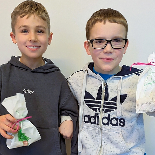 Zwei Jungen halten kleine Geschenktüten in den Händen und lächeln in die Kamera. Die Tüten sind mit Zeichnungen und Schleifen verziert.